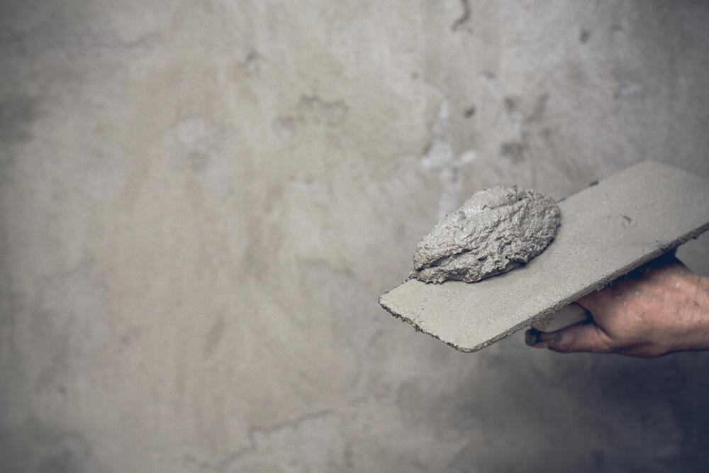 Hand holding a tool with a small pile of cement to be smeared on an interior wall.