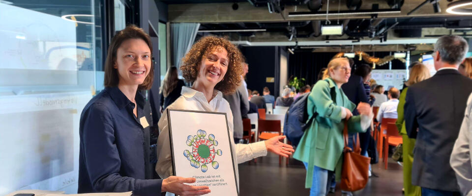 Zwei Frauen halten ein Schild mit dem Umweltzeichenlogo.