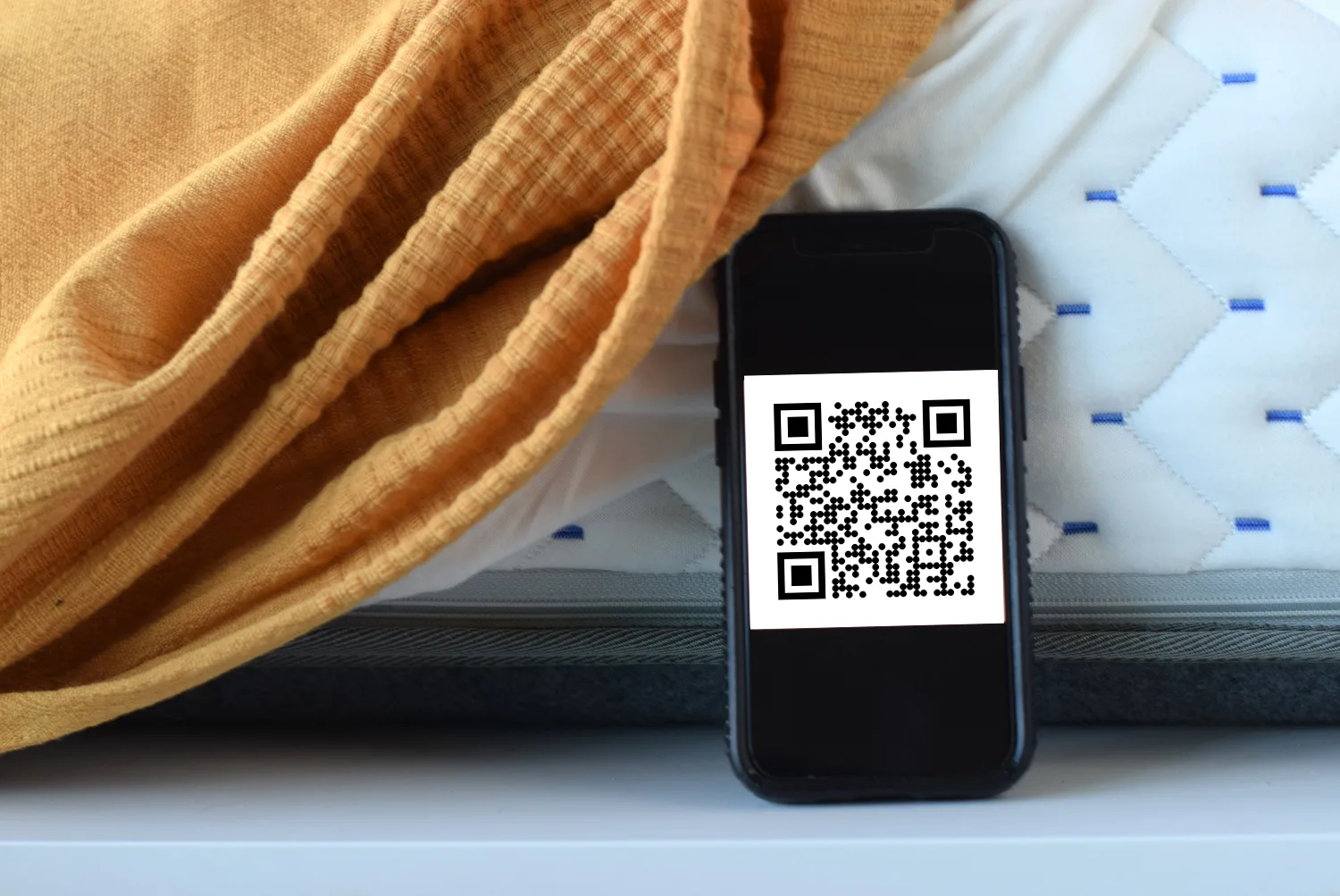 Handy mit QR-Code vor einem Matratze
